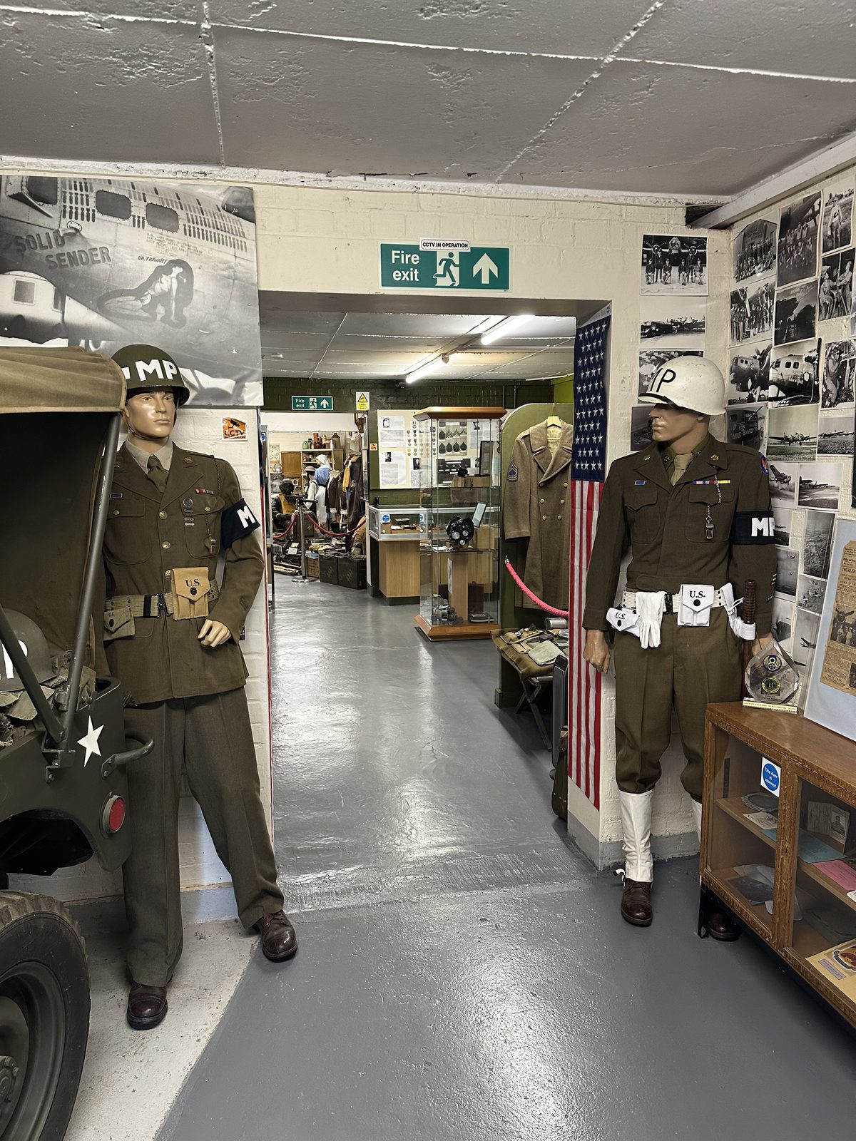 Two military police mannequins in white helmets marked MP standing either side of a doorway, beside a large photograph of the B-17 nose art Solid Sender.
